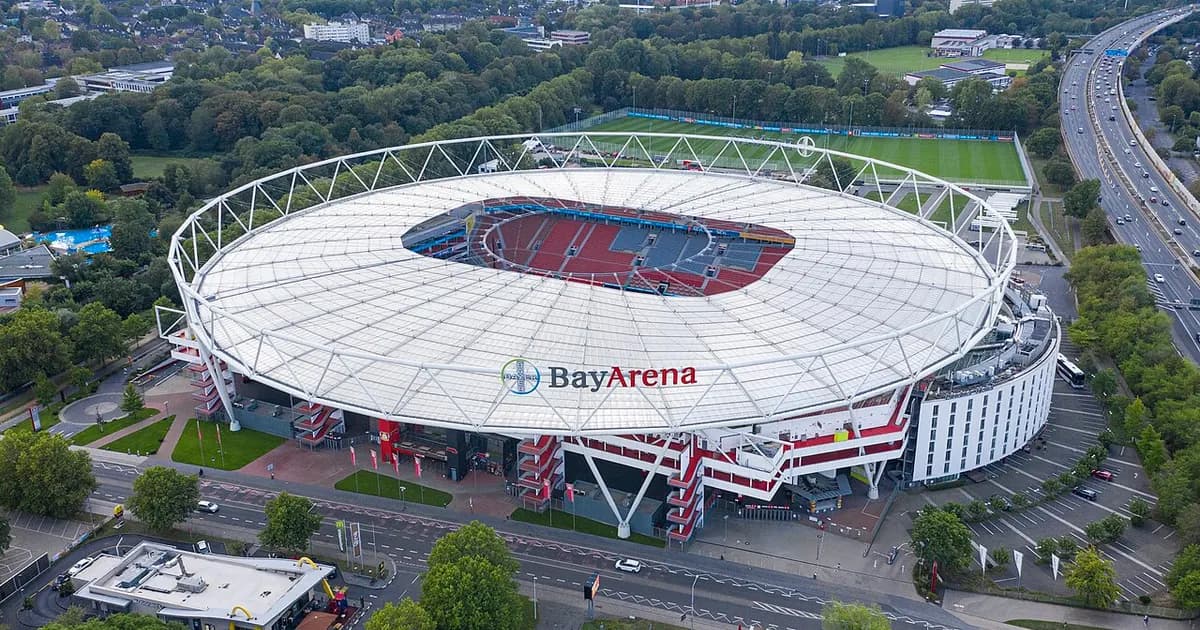 Ein Fußballstadion kurz vor Anpfiff, mit leeren Rängen und grünem Rasen im Abendlicht