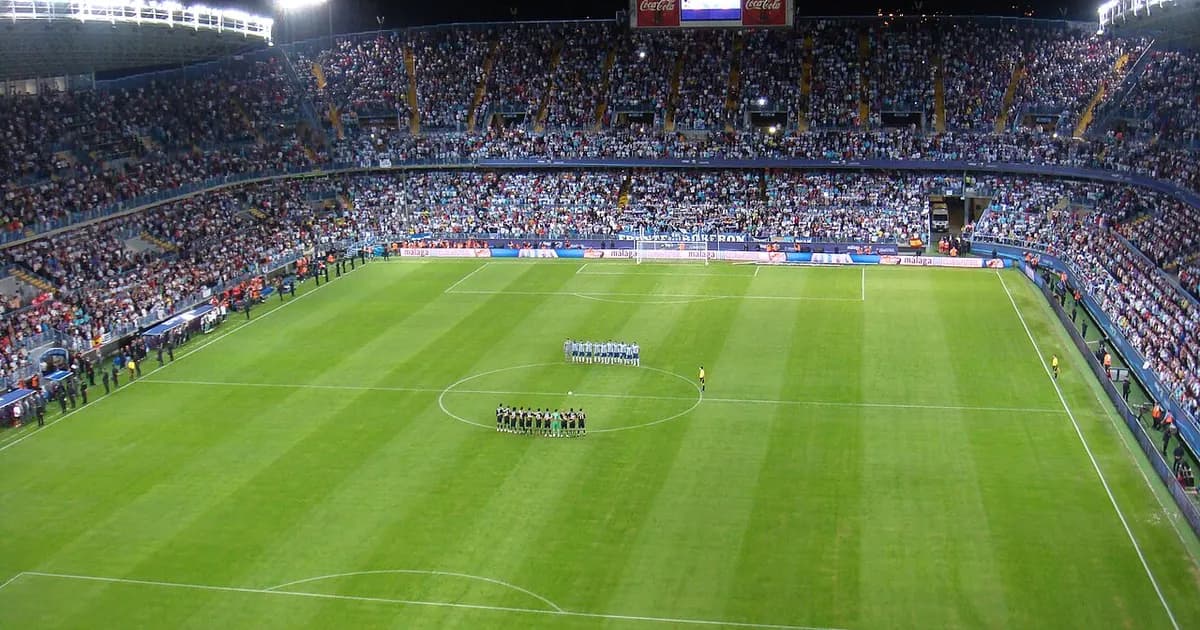 A packed La Rosaleda stadium in Málaga filled with supporters before the match begins, with the pitch prepared and team lineups ready to take the field for the LaLiga encounter against Espanyol.