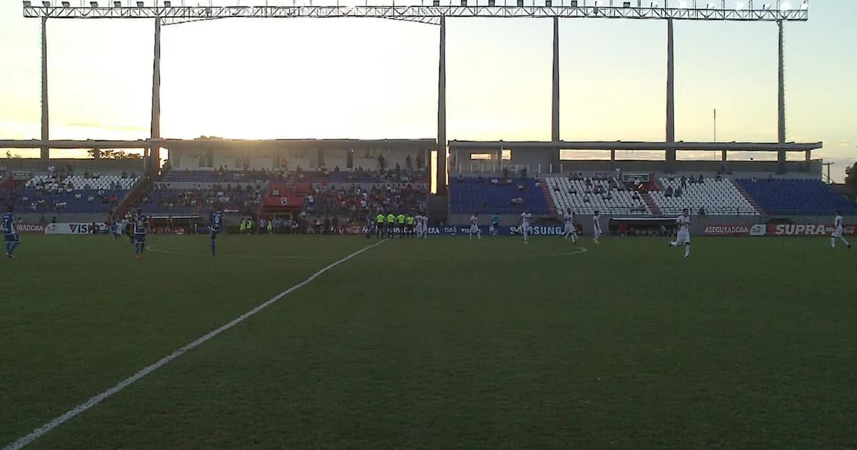 Football stadium with green pitch, blue sky, and white stadium seats before the Nacional Asunción vs Deportivo Recoleta match.